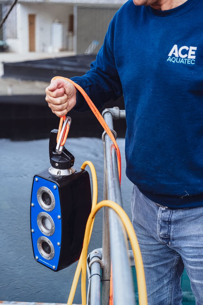 A man holds a machine over some water.