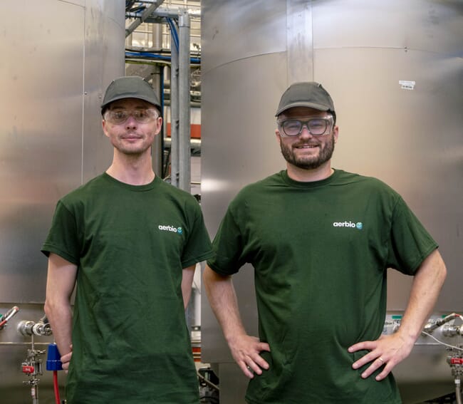 two men stand in front of two large metal containers