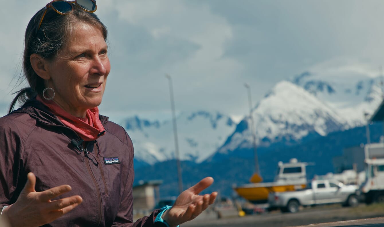 A woman talking in front of snowy mountains.