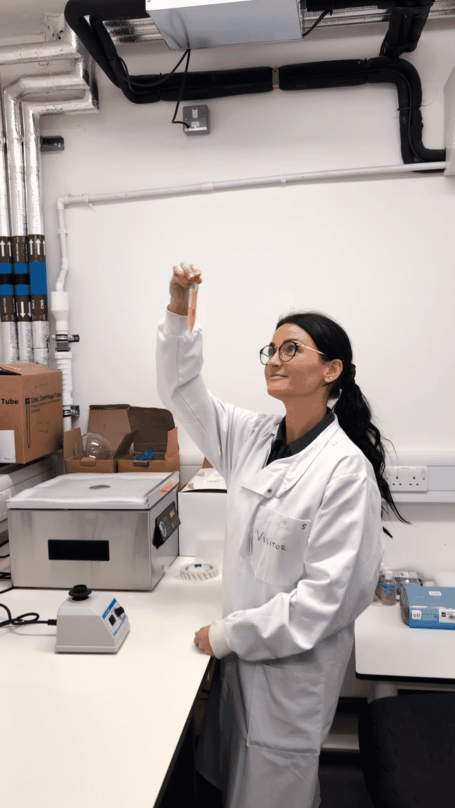 Uma mulher em um jaleco de laboratório examinando um tubo de ensaio.