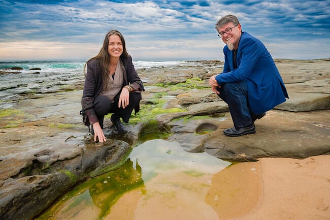 Two people squatting in the intertidal zone examining seaweed growing on rocks