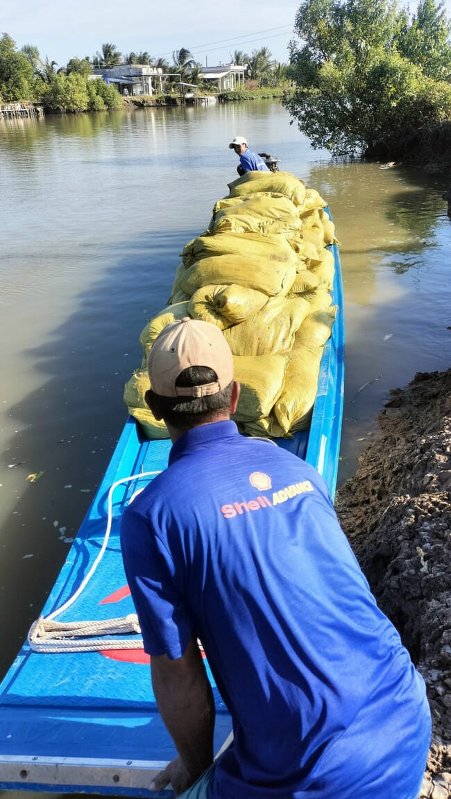 A man in a boat laden with bags of seaweed.