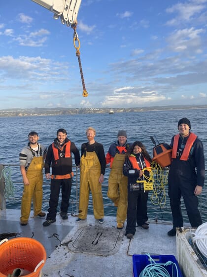 A group of people in wet weather clothing beside the sea.