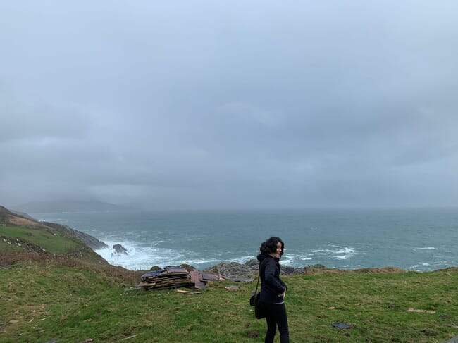 a woman stands on a rugged coastline