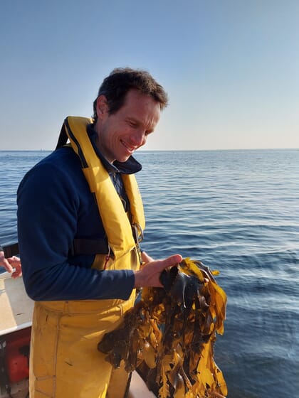 Man standing in waders holding a clump of seaweed