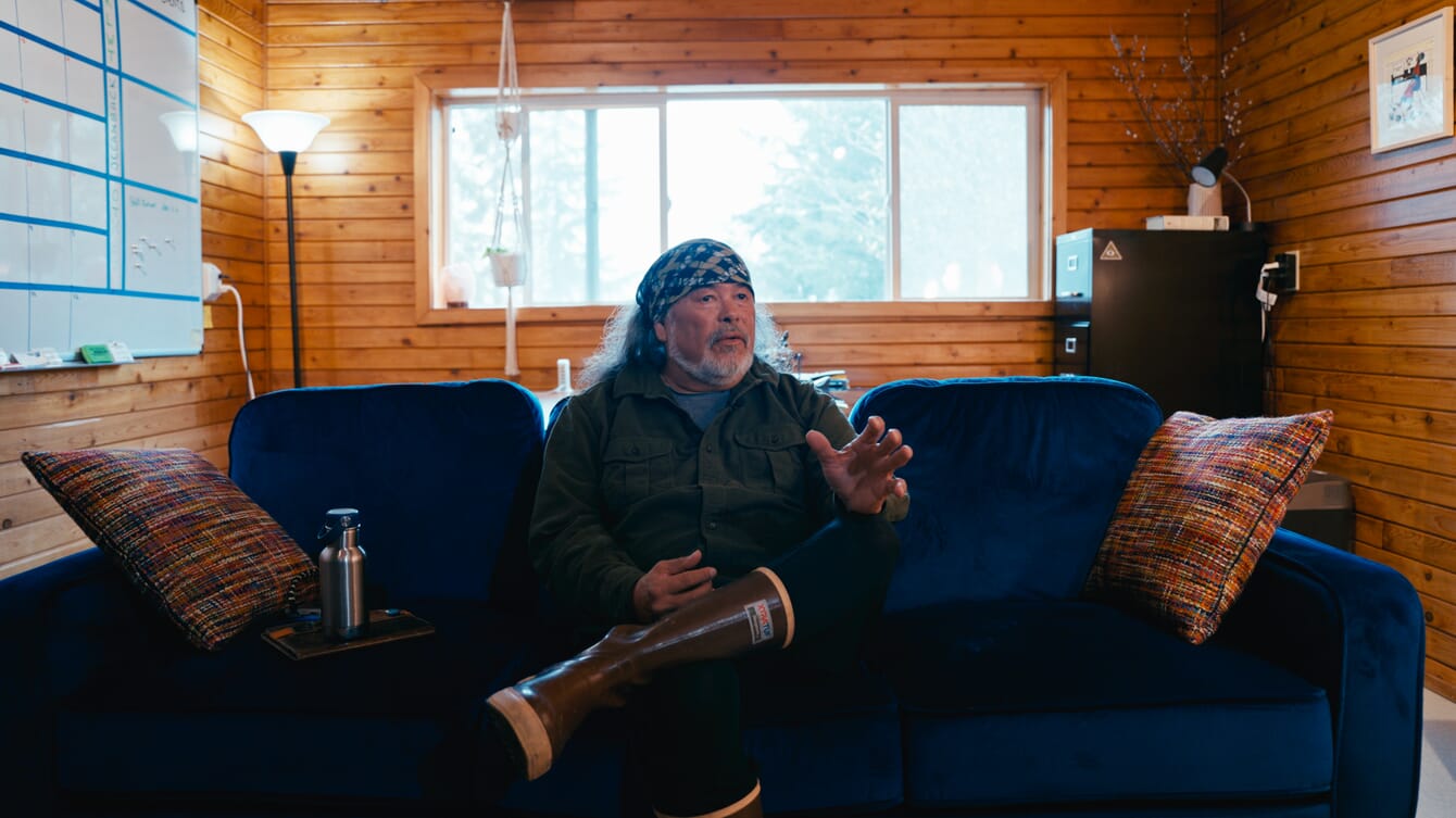A man sitting on a sofa inside a wood-panelled office.