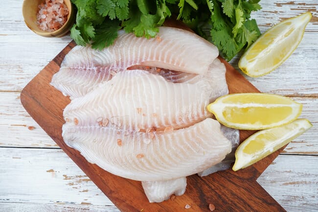 Two pieces of fish on a chopping board.