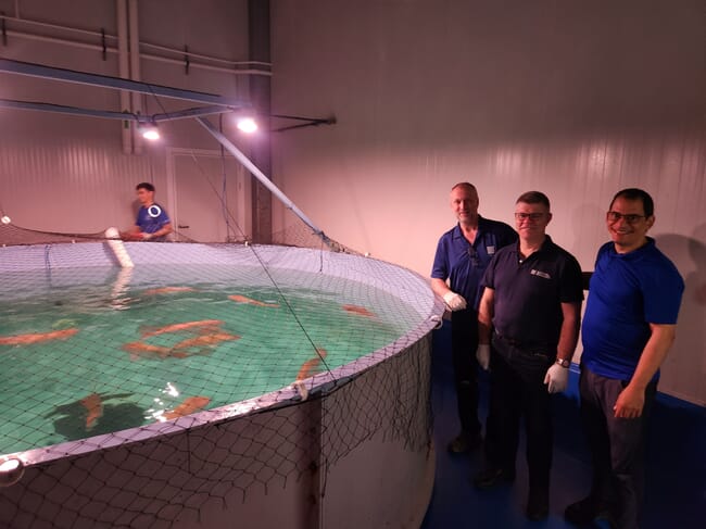 Três homens em pé ao lado de um grande tanque de peixes.