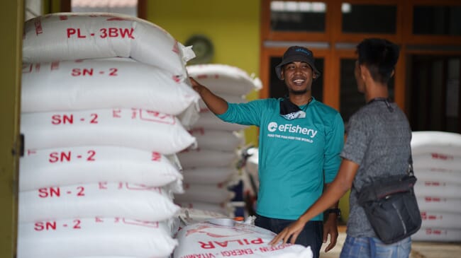 a smiling man beside some feed bags