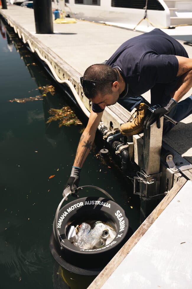 Homem retirando uma lata de lixo da água em um porto