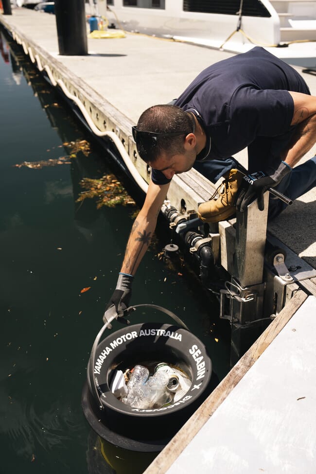 Man pulling bin of trash from the water in a harbour