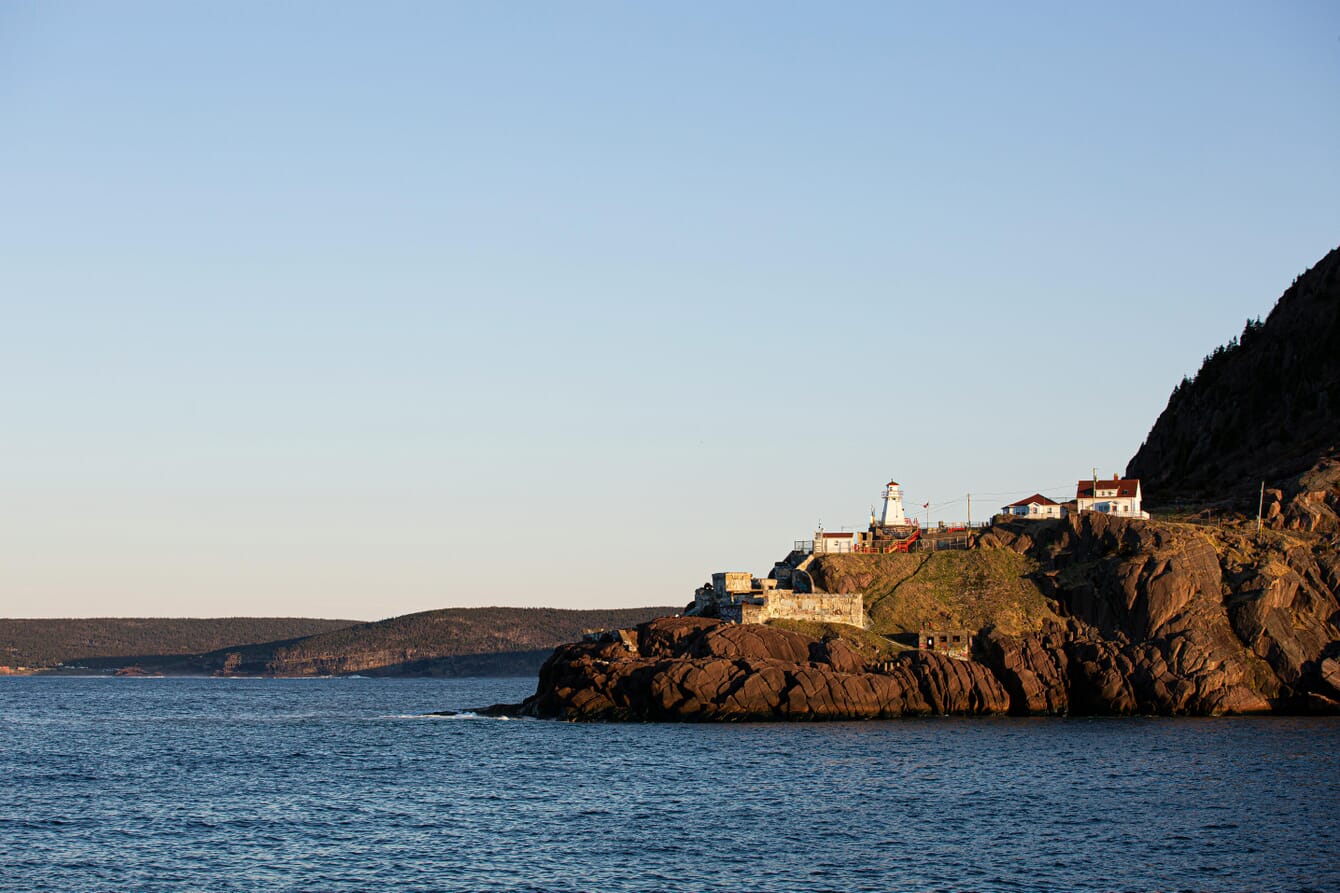 A cliff in Canada with a white and red lighthouse.