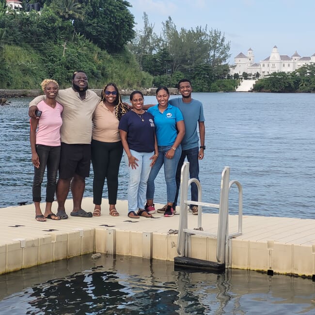 Um grupo de seis pessoas em pé em uma estrutura flutuante no mar.