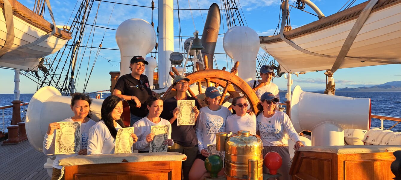 A group of women on a tall ship at sunset.