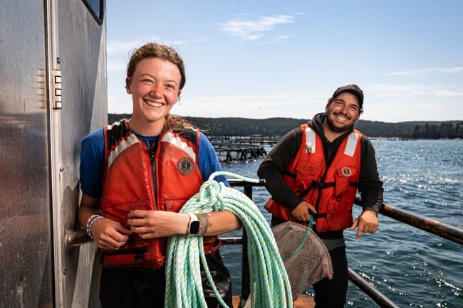 a girl stands in front of a man on the edge of a lake holding a rope and smiling