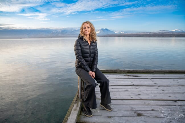 Nofima senior scientist, Elisabeth Ytteborg sitting on a dock in a coat in a Norwegian fjord.