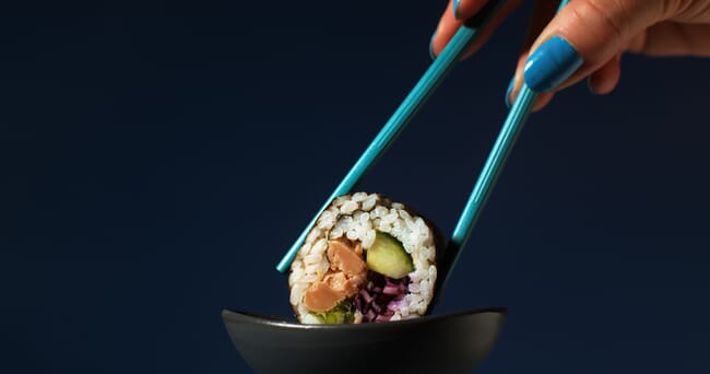 Sushi roll with Oridinary Seafood tuna being held by chopsticks in a sauce dish.