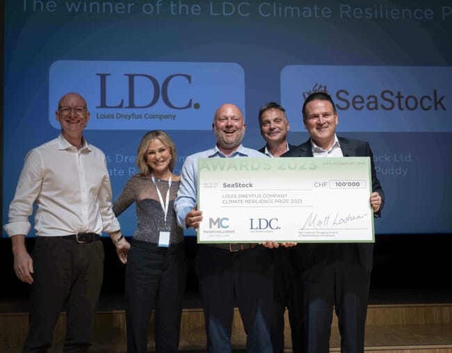 SeaStock team stands on stage and holds large cardboard check for 100,000 Swiss Francs.