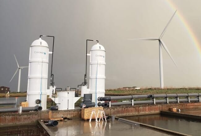 A water treatment unit on a cloudy day near a wind turbine.