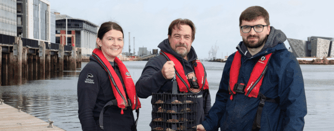 three people holding a small cage containing oysters