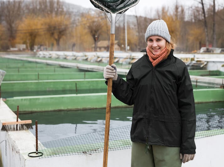 A female fish farmer standing beside a fish farm, holding a net