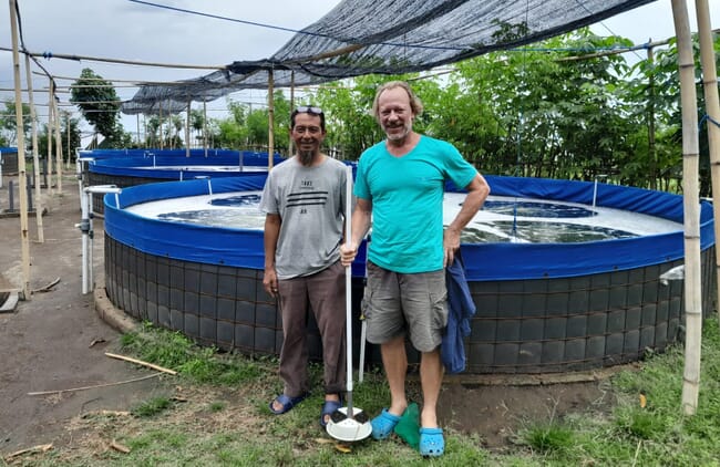 Two men standing in front of a raised pond at a fish farm