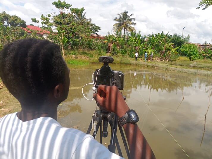 a man  filming a farmer beside a pond
