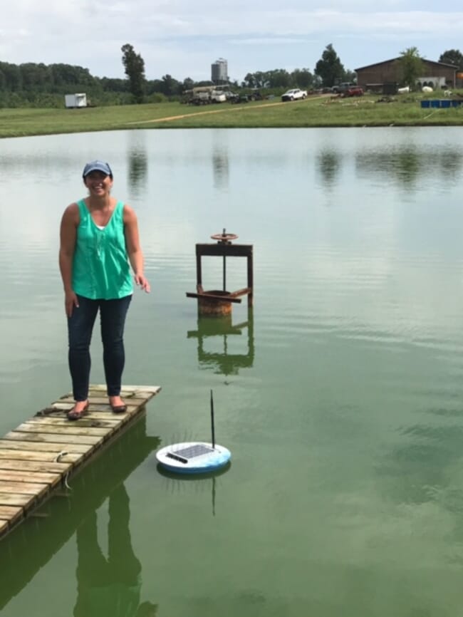 A woman standing on a jetty beside a pond.