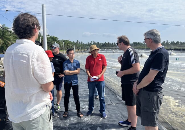 Group of men talking next to a shrimp pond