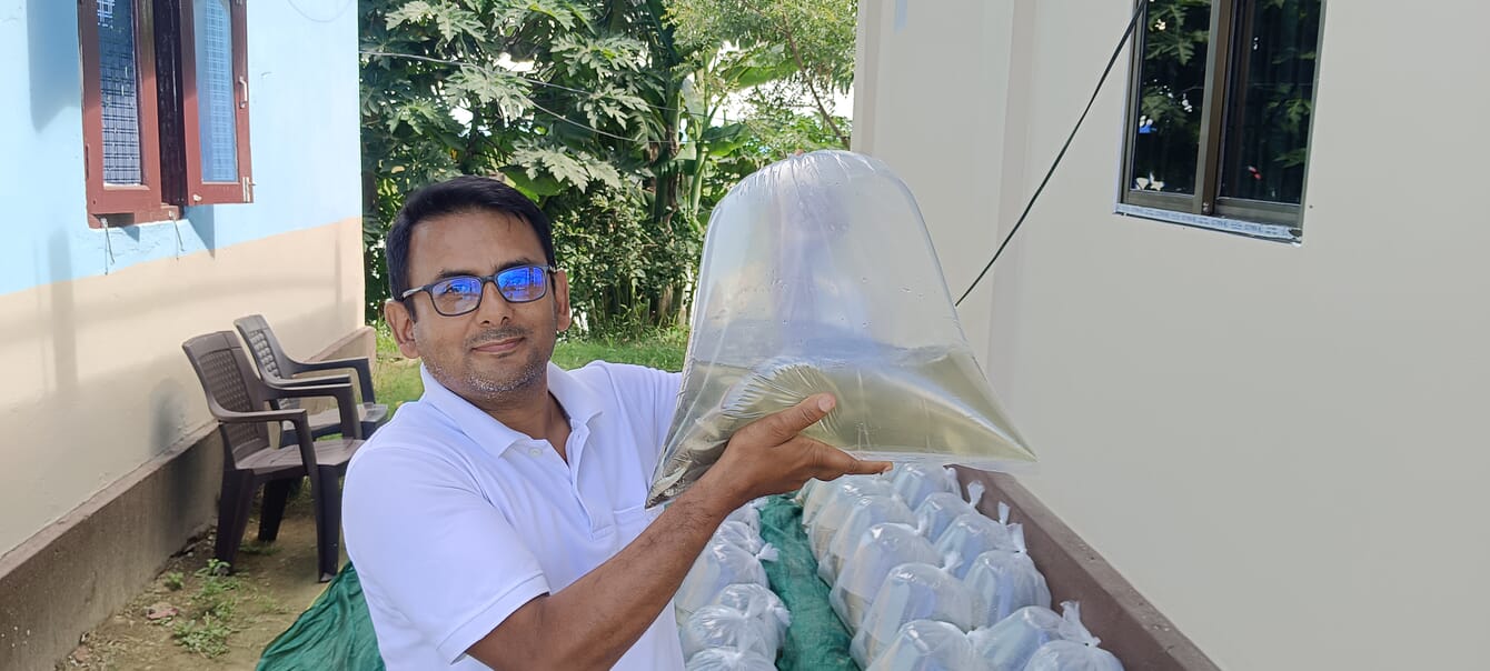 A carp farmer holding a bag of carp fry up in the air, infront of his farm.