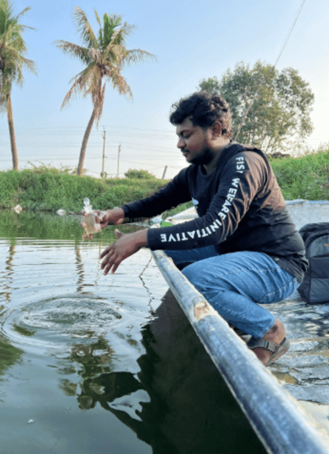 A man squatting beside a pond.