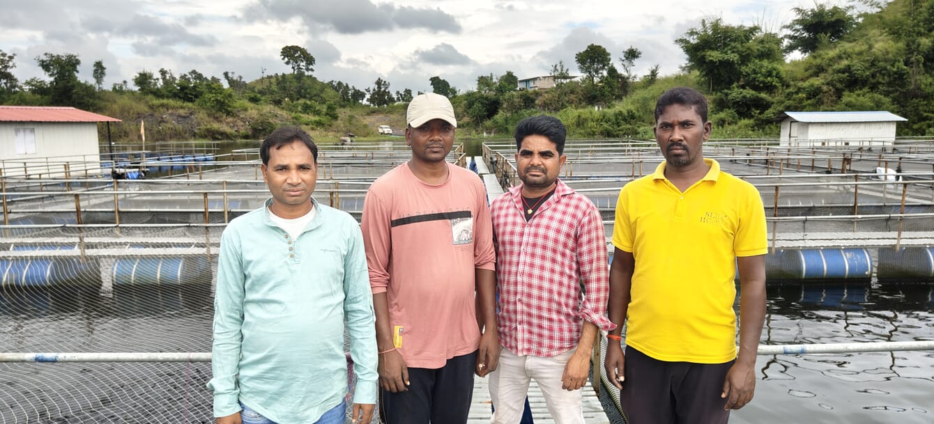 Four men standing on fish cages in a lake.