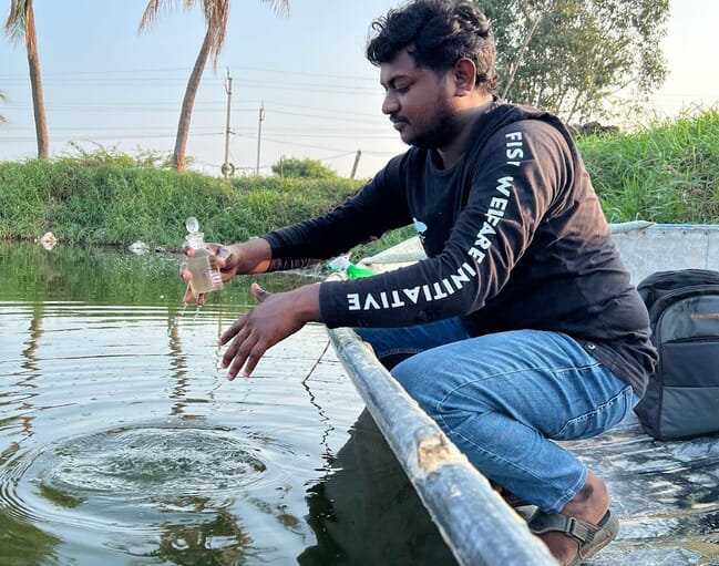 A man squatting beside a pond.