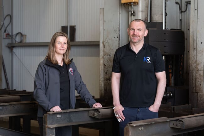 a woman and a m an stand in a shed. the woman is leaning on iron pillars that are around them