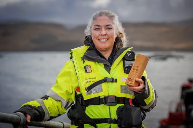 a woman stands on the edge of some water holding an award and smiling