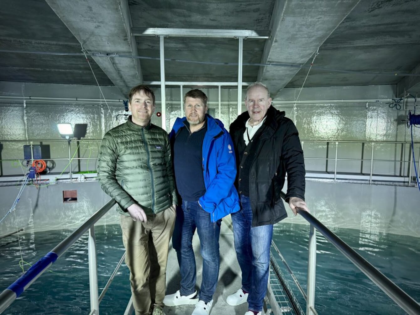Three men standing in an indoor salmon farm.