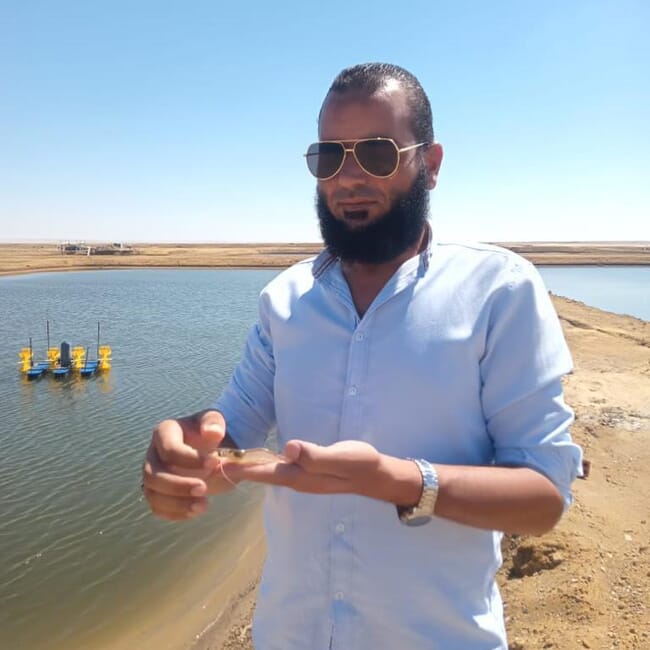 Man standing next to a pond at a shrimp farm