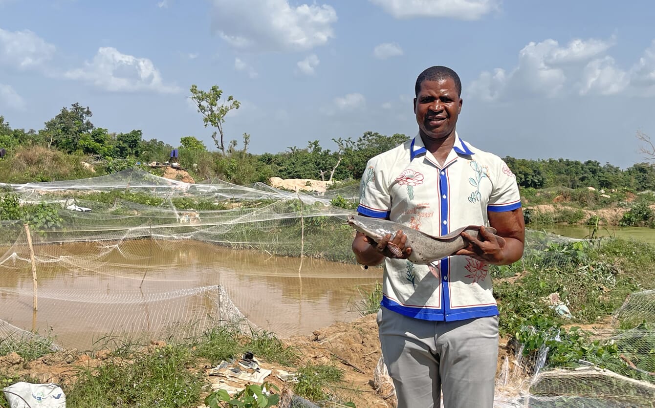 Man holding a catfish next to a pond