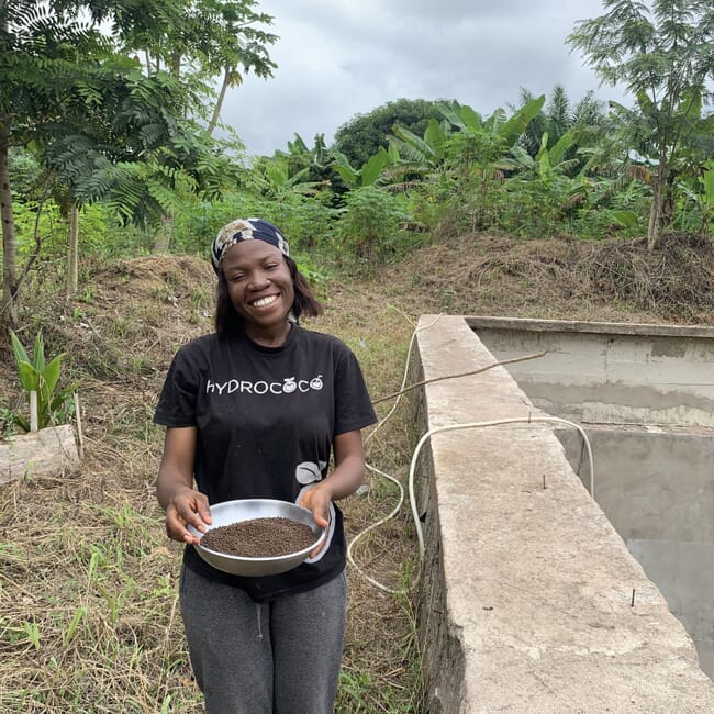 Smiling woman next to concrete pond holding bowl of fish feed