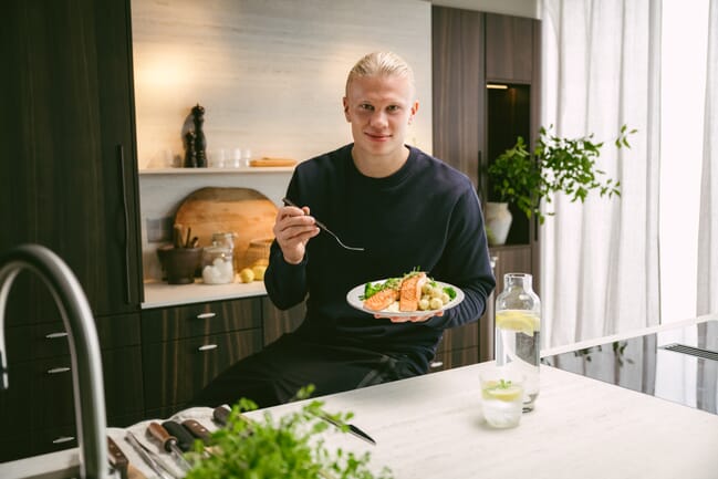 A man holding up a plate of salmon in a kitchen.
