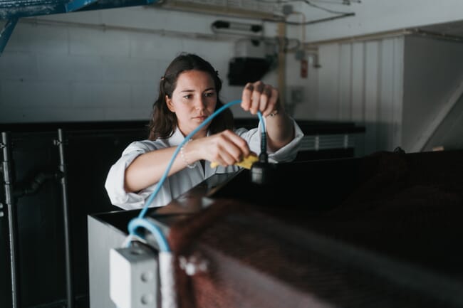 A person in a lab coat checking a fish tank.