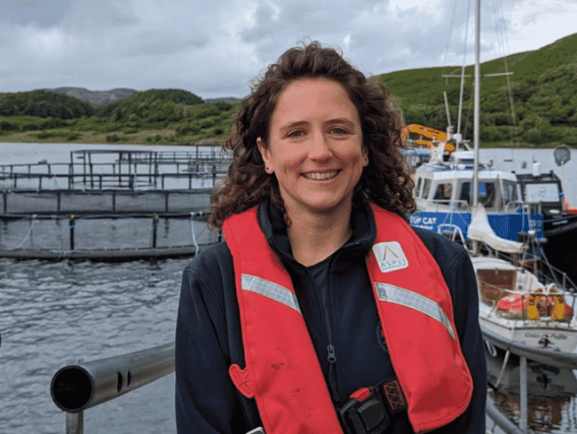 a woman wearing a lifejacket, beside a salmon farm