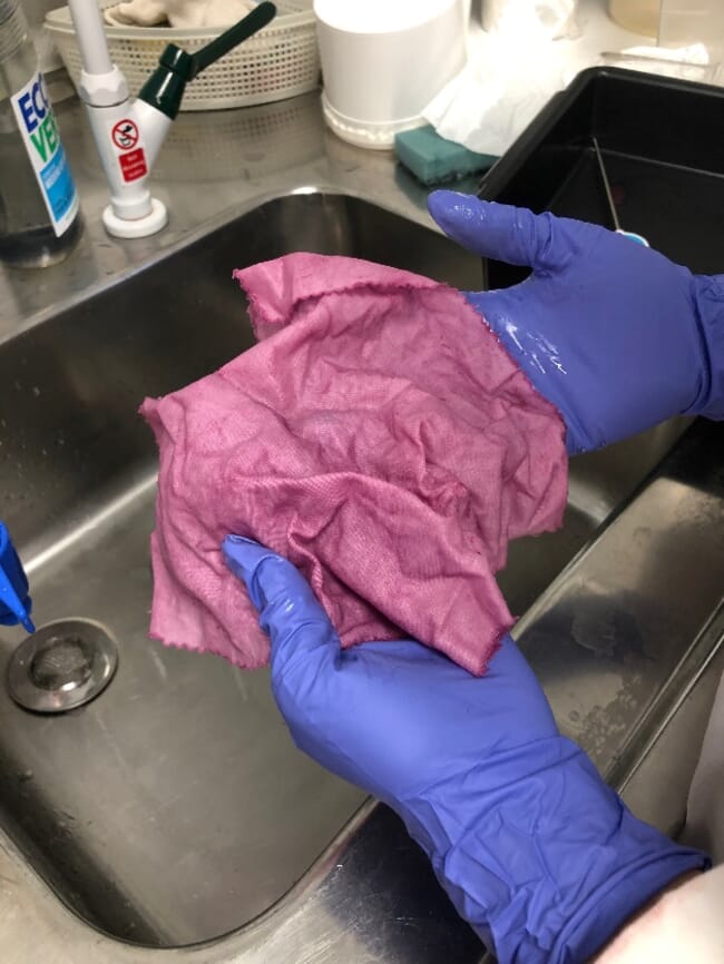 A person holding a pink cloth above a sink.