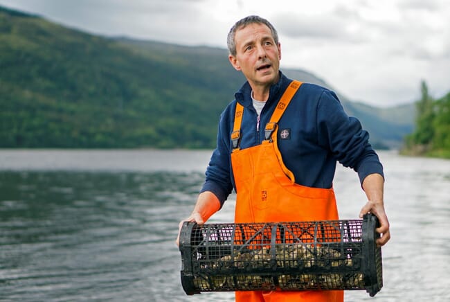 A man holding a freshly collected basket of oysters from Scotland.