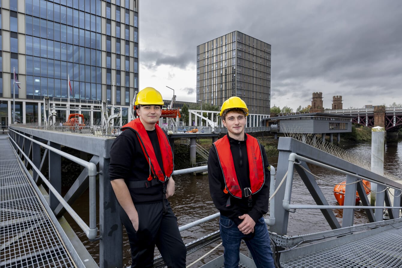 Two young men standing on the port of Glasgow wearing maritime equipment.