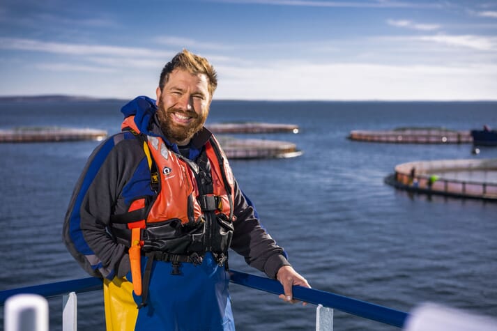 a smiling bearded man standing on the edge of a salmon pen