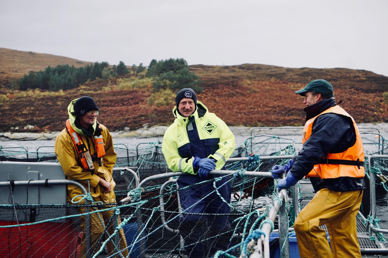 Three men on an Atlantic salmon farm in Scotland on a cloudy day.