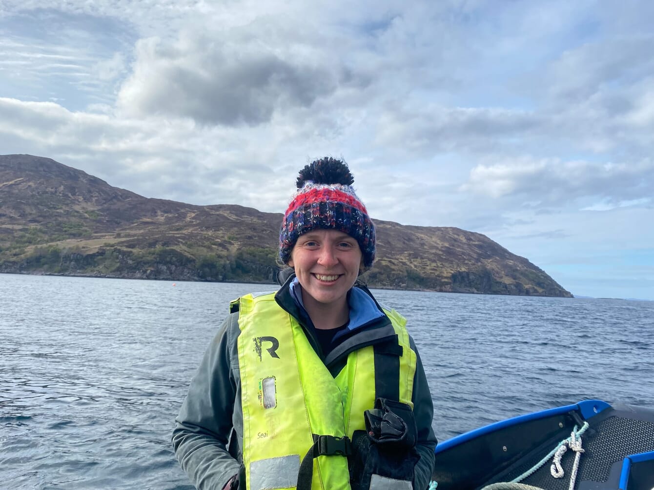 Portrait of smiling woman on a boat wearing a bobble hat and high viz life vest