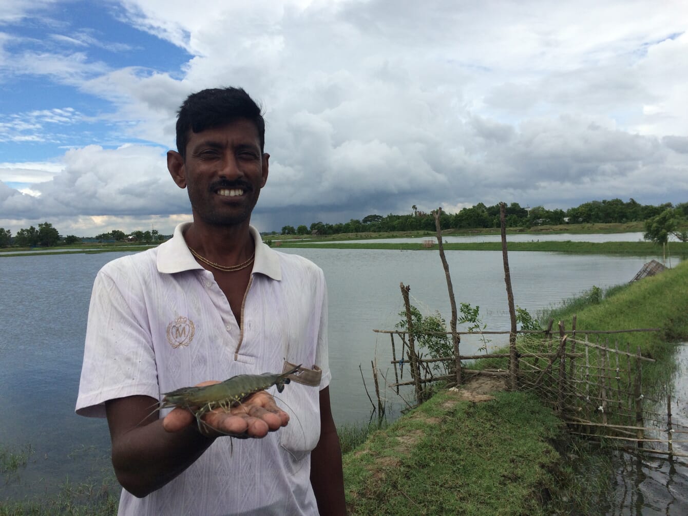 A man holding a shrimp in front of a pond.