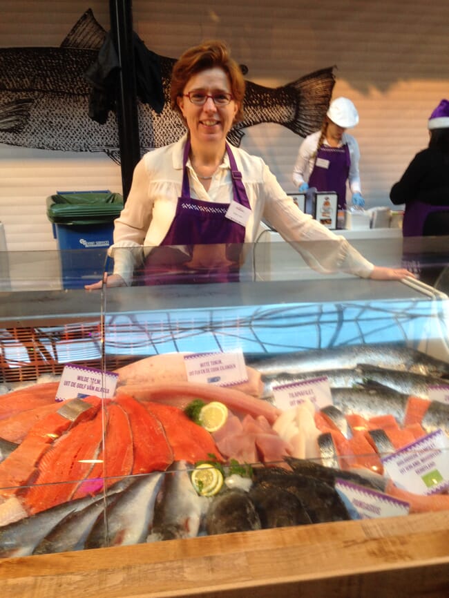 A woman in an apron standing behind a fish counter.